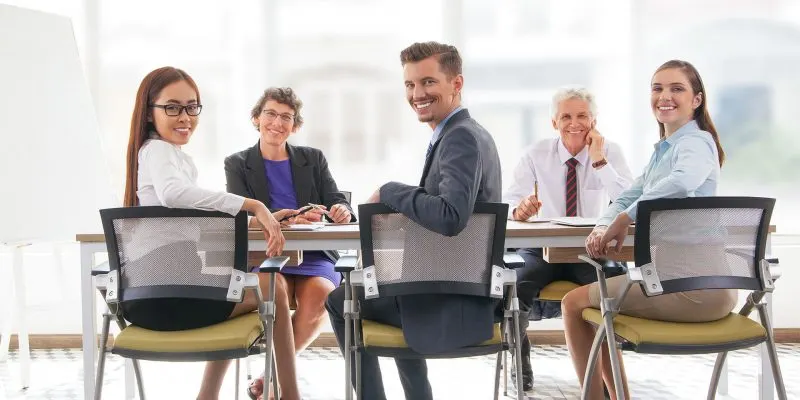 Multi-ethnic smiling business team sitting at table and looking at camera. Business executives having meeting in office. Teamwork concept